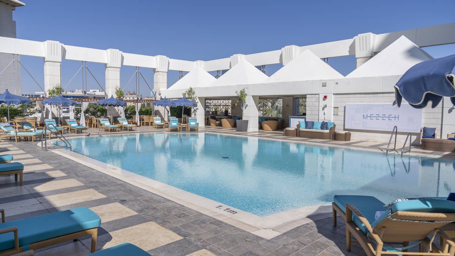 Outdoor pool surrounded by blue lounge chairs and four white tents
