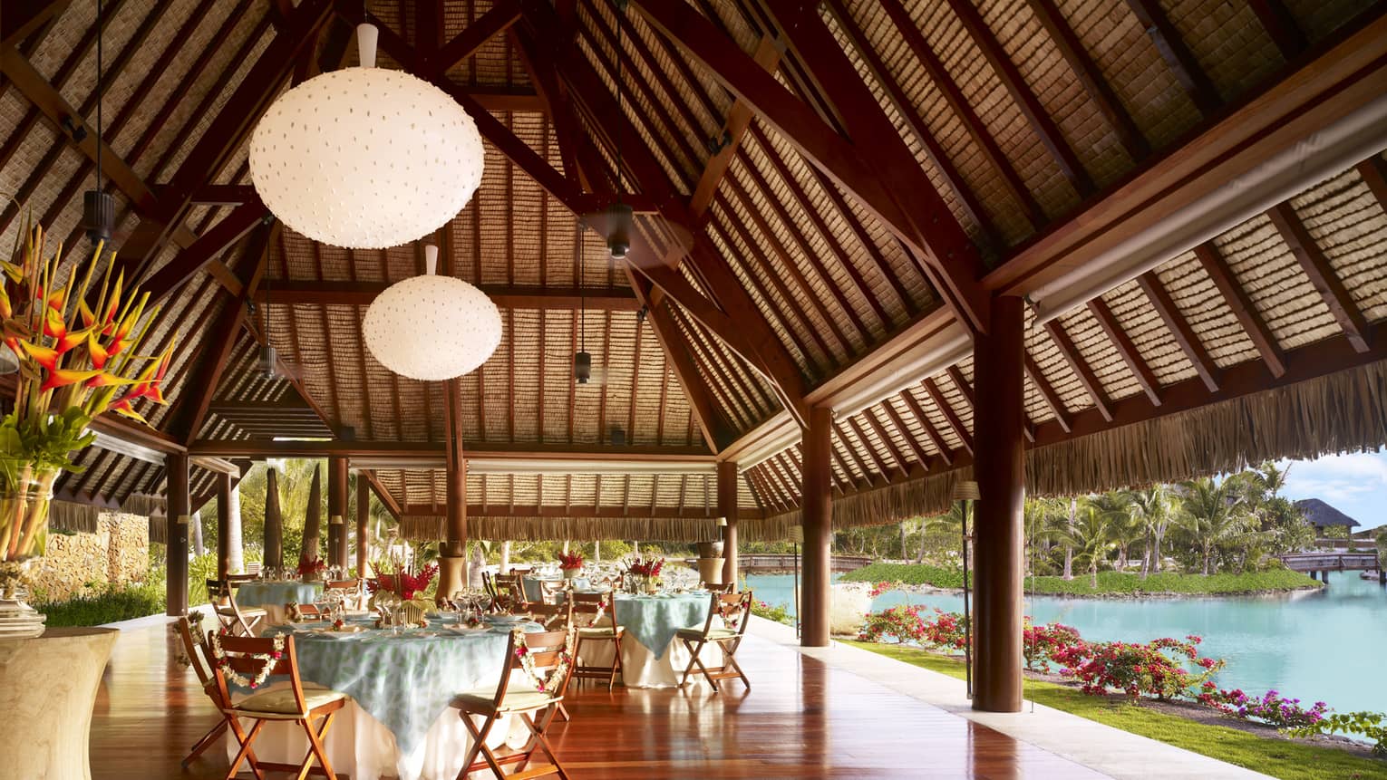 Large globe lanterns over round banquet tables in Otemanu outdoor pavilion by water