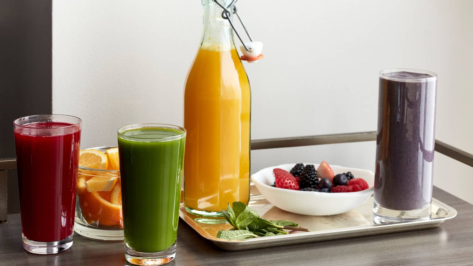 A table filled with various smoothies, a fruit bowl, and a bottle of orange juice