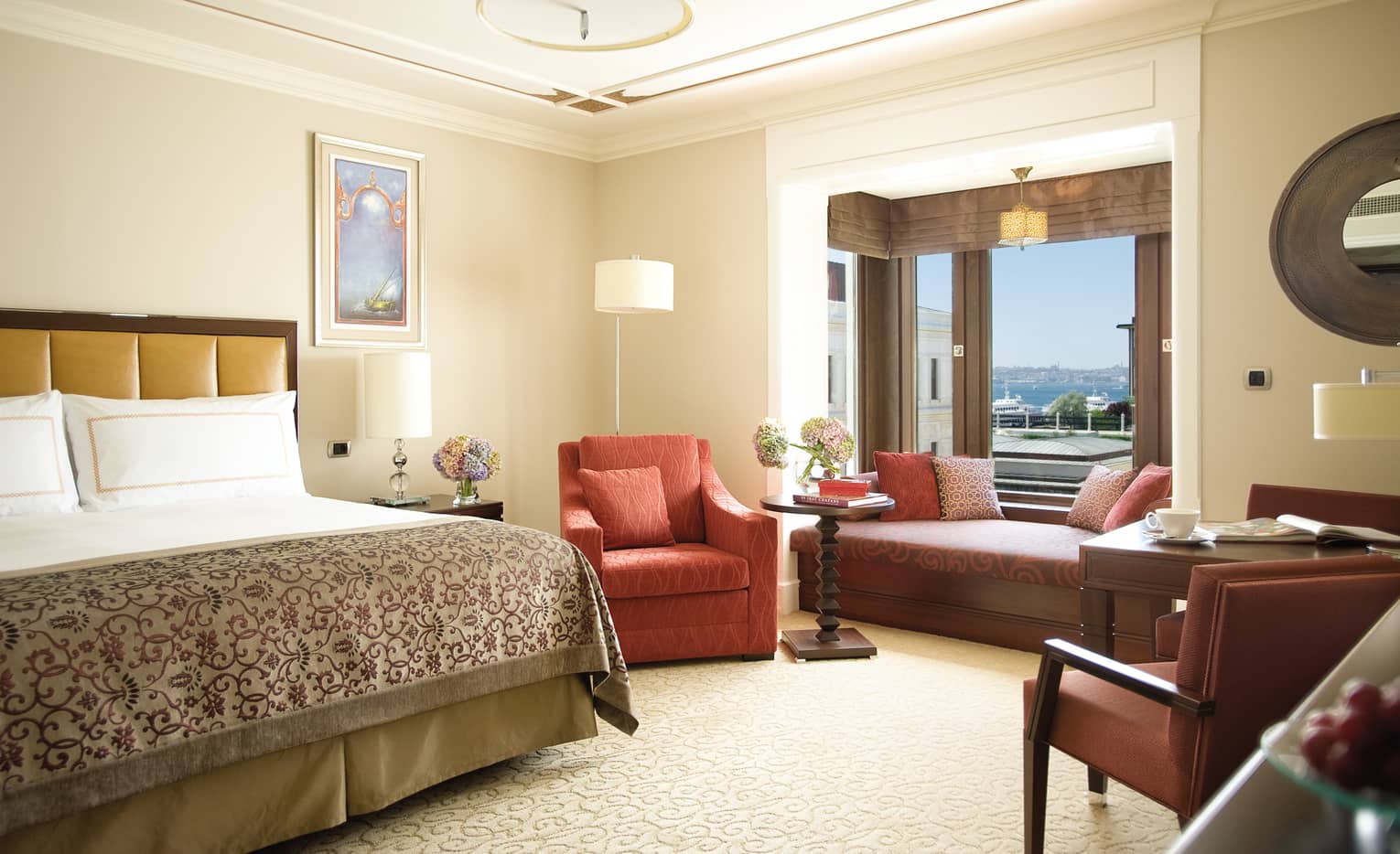 Deluxe Room bed with patterned blanket, red armchair, padded bench under window
