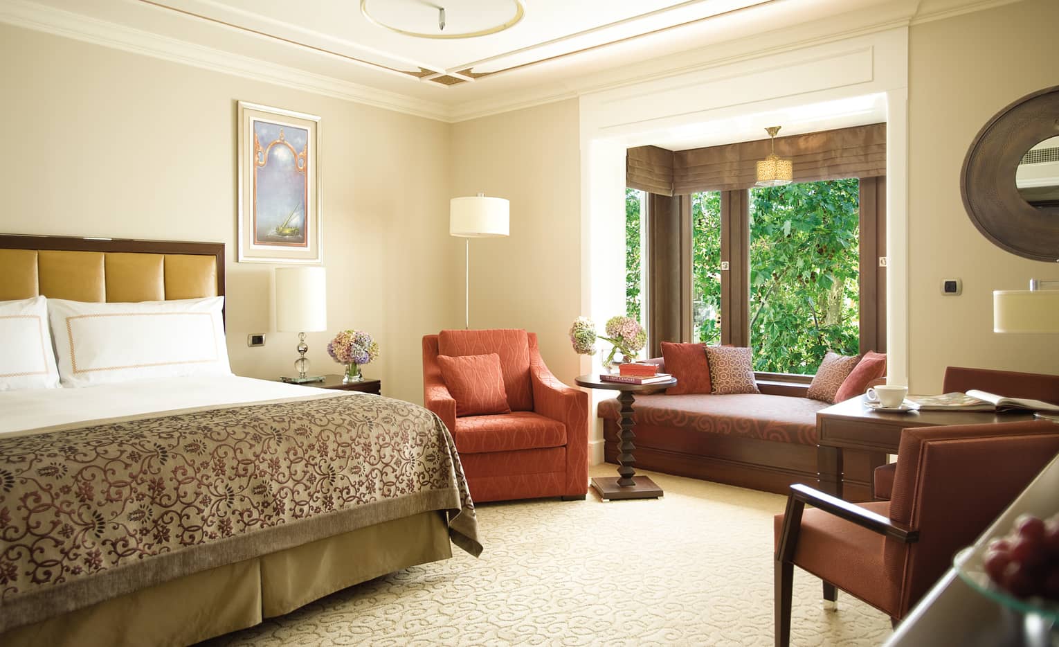 Superior Room bed with patterned blanket, red armchair, padded bench under window