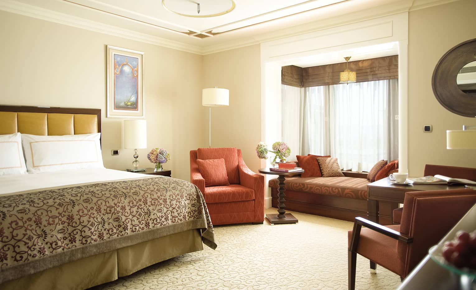 Deluxe Room bed with patterned blanket, red armchair, padded bench under window