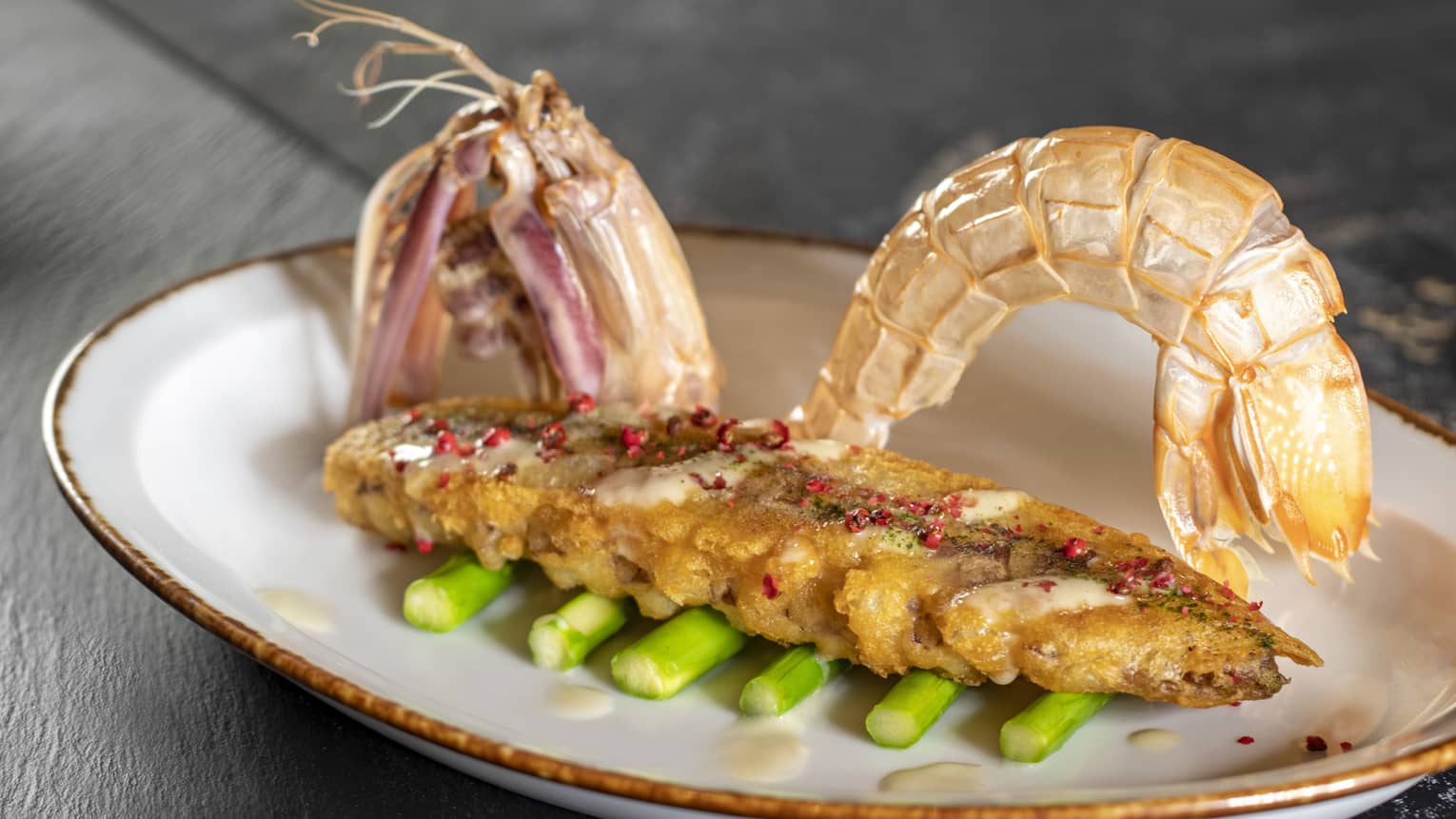 Shell-on prawns on bed of asparagus spears in oval white dish with gold rim