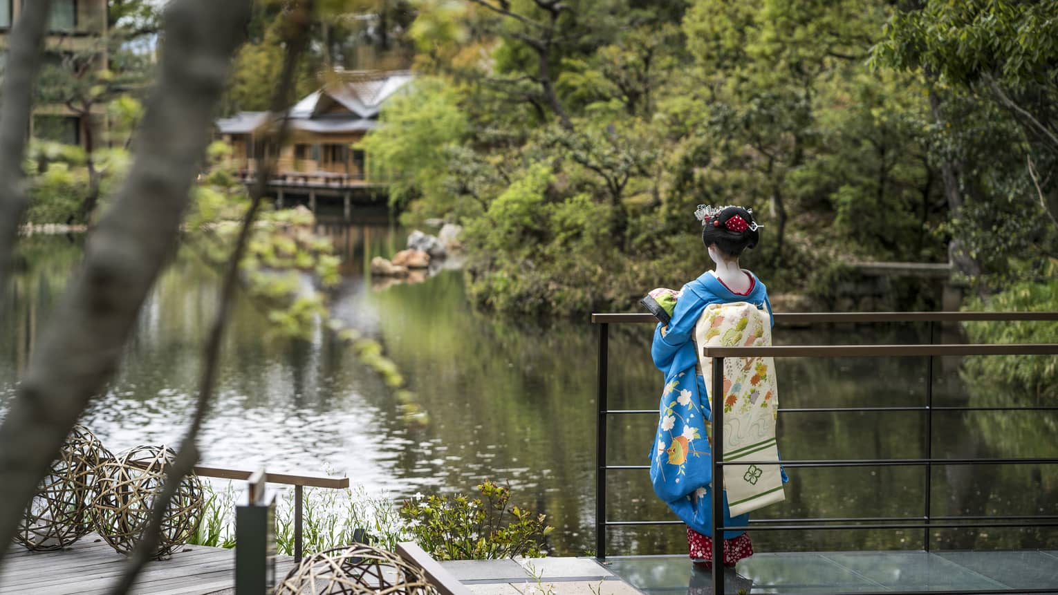 Person in a traditional blue kimono standing by a pond with lush greenery