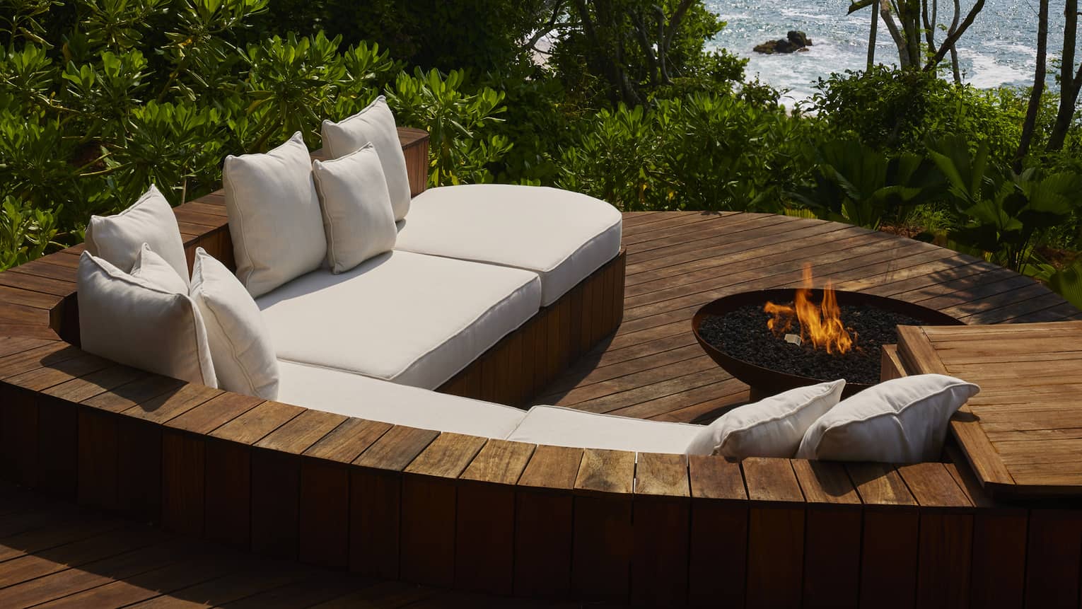 A sunken wooden patio with sofa and firepit, jungle and ocean view