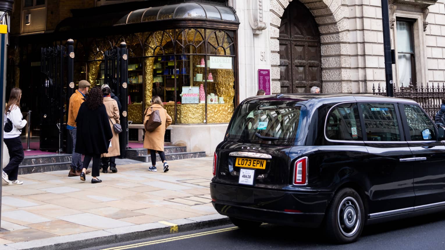London-style black cab parked in front of a high-end pastry shop in a building with a Burlington Arcade sign and flag.