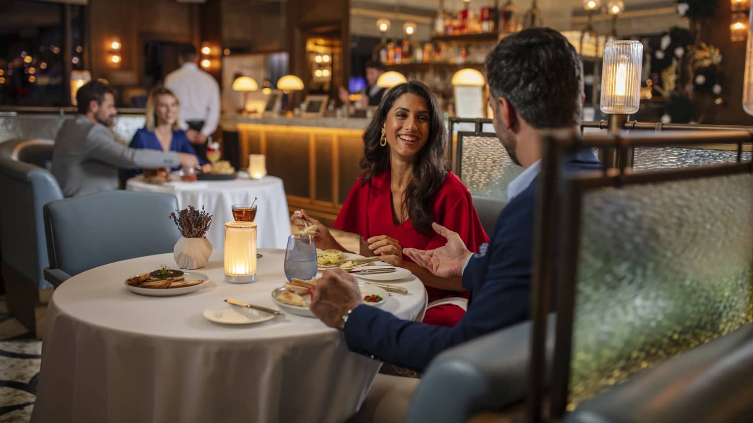 Woman in red dress, smiling at man, seated at round dining table in bar lounge