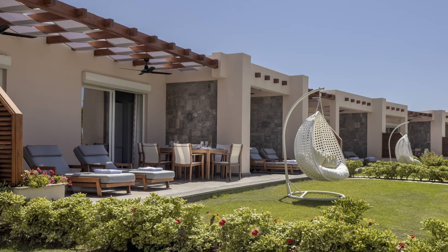 Suite patio and yard with blue lounge chairs and white egg chair, shrubbery