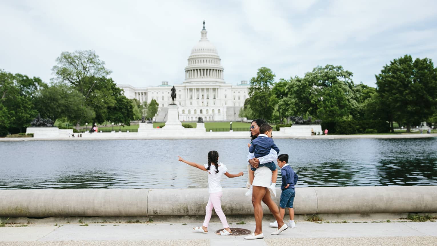 Woman and three children walk in front of the Capitol reflecting pool in Washington, DC, with Capitol building in background