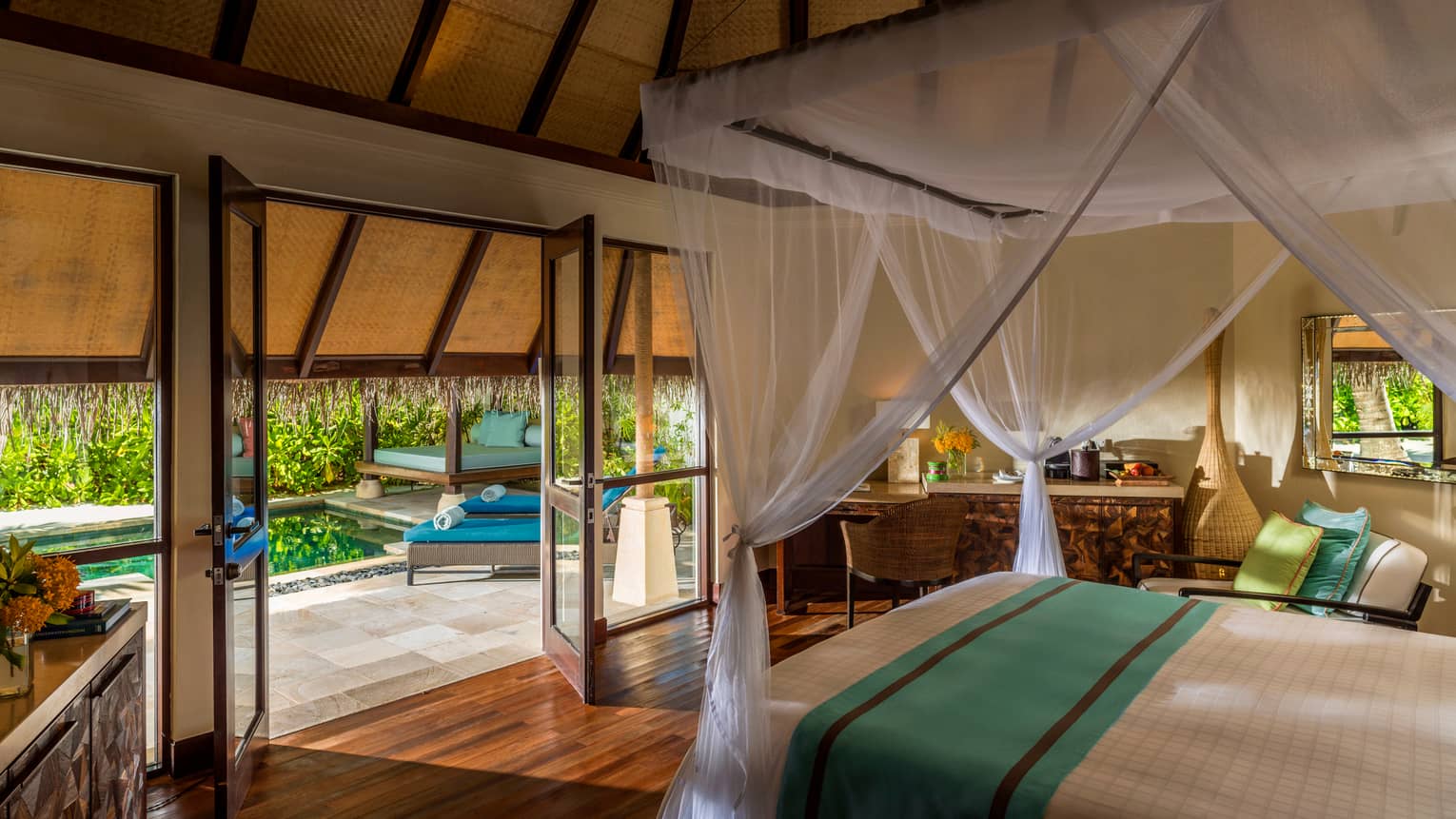 Traditional beach pavilion suite with canopy bed and open-air doors and windows leading to patio