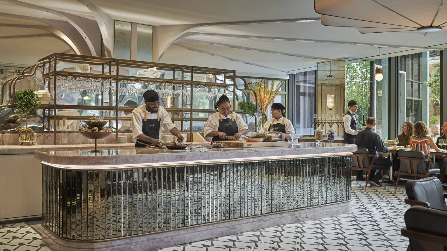 Three staff members prepare dishes behind the counter at Miss River, a table of guests being served in the background