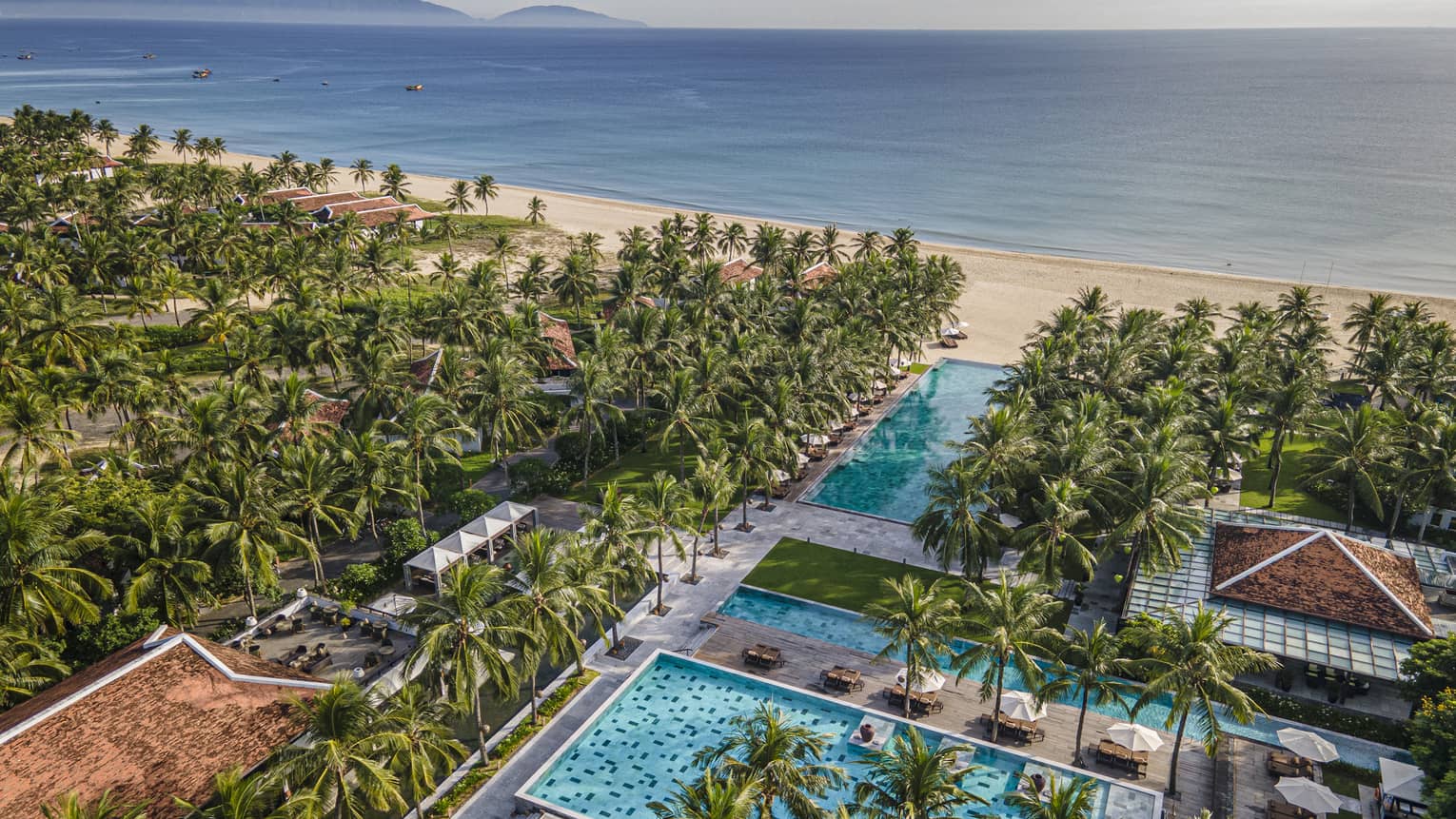 Aerial view of the resort pools with ocean views, palm trees and blue skies