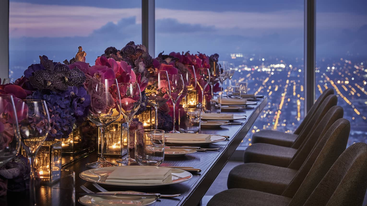 A banquet style table is decorated with tea candles, white plates, pink flowers and overlooks downtown Philadelphia 