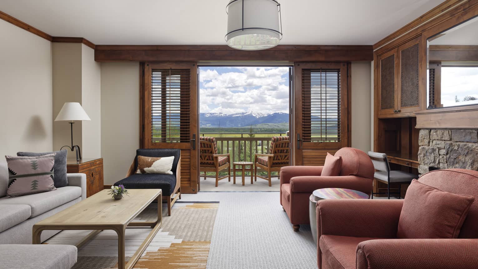 Living room with a sofa, two red armchairs, wooden coffee table, and a balcony door opening to a scenic mountain view
