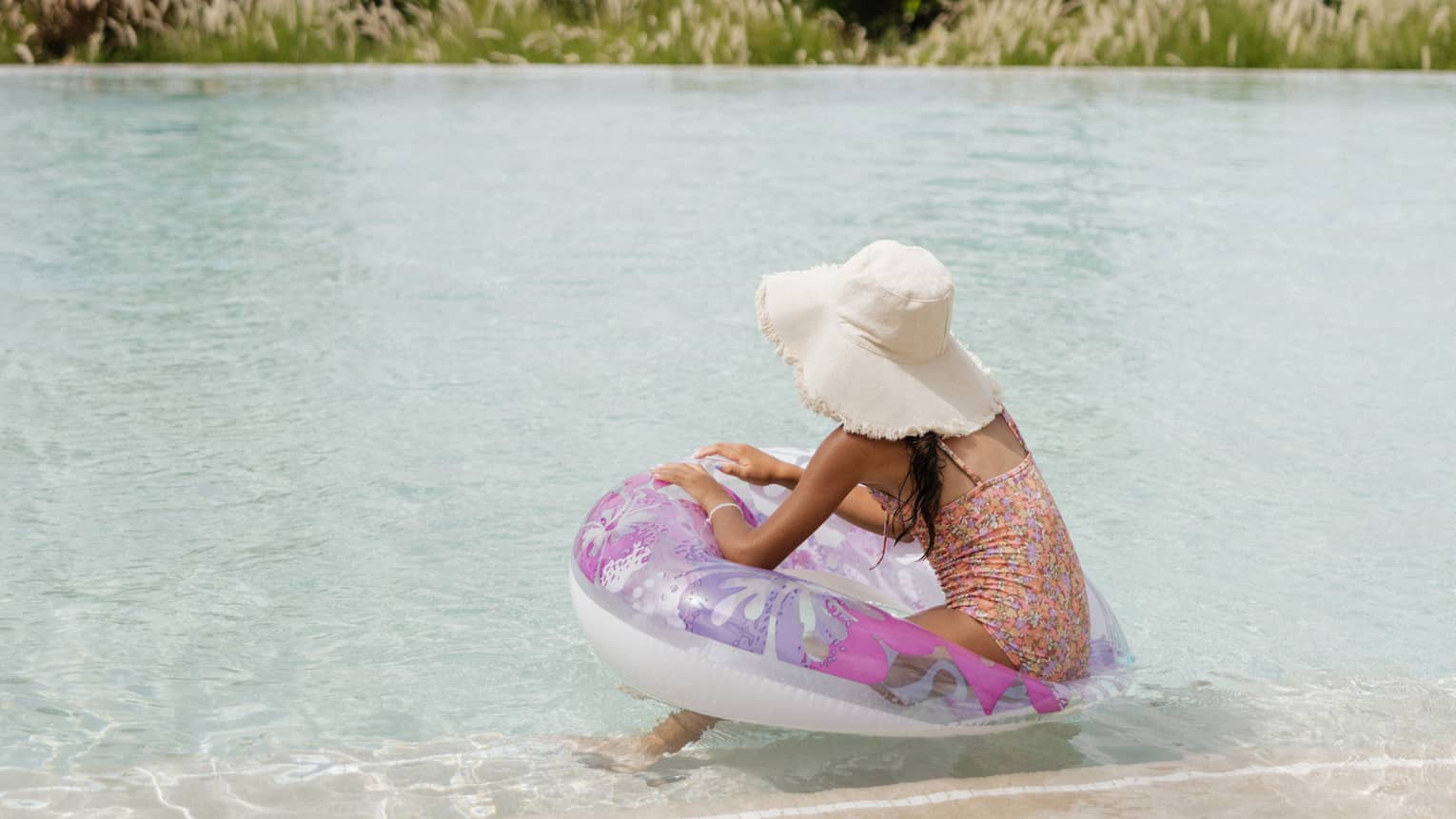 Young guest on a purple float in the water with the ocean and palm trees in the background.