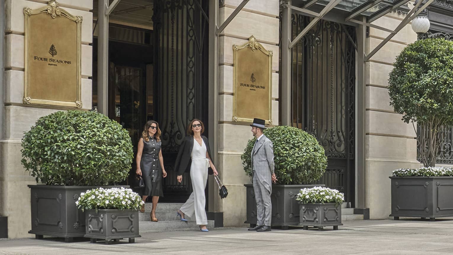 Four Seasons luxury hotel entrance with two guests walking out, doorman, glass canopies and large potted plants