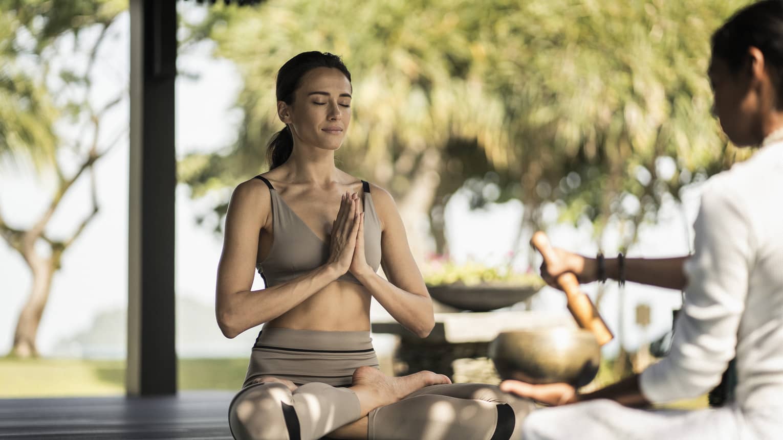A woman sitting outside doing a yoga breathing pose.