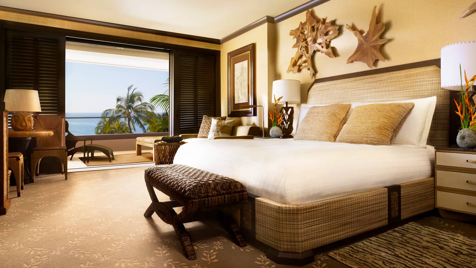 Penthouse Deluxe Oceanfront Suite bed with rattan frame, bench, rustic wood wall hangings, open wall to balcony