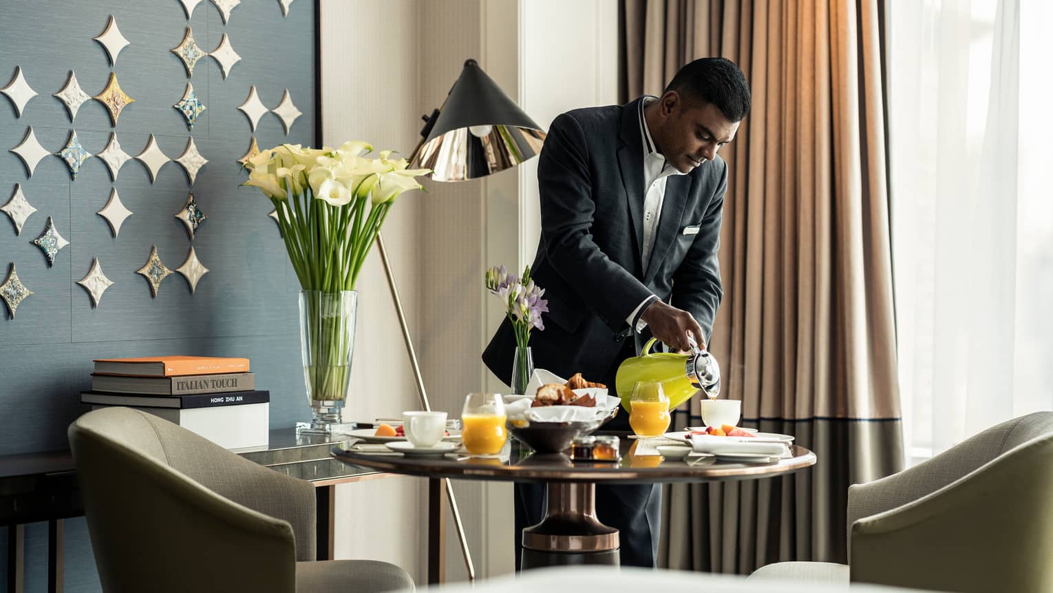 Hotel staff pours coffee from carafe into cup on brunch tray on in-room dining table