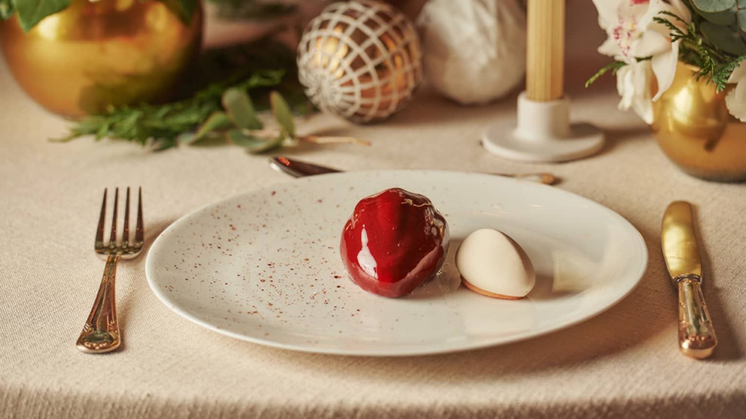Modern, glossy, red ice cream dessert on a plate, with festive ornaments as decoration on the table