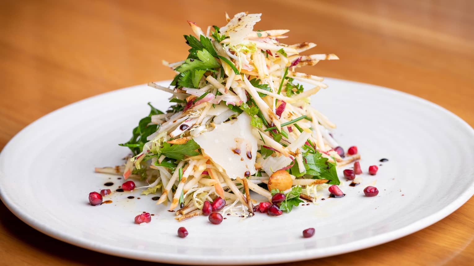 Close-up of entree with greens, julienned vegetables, pomegranate seeds