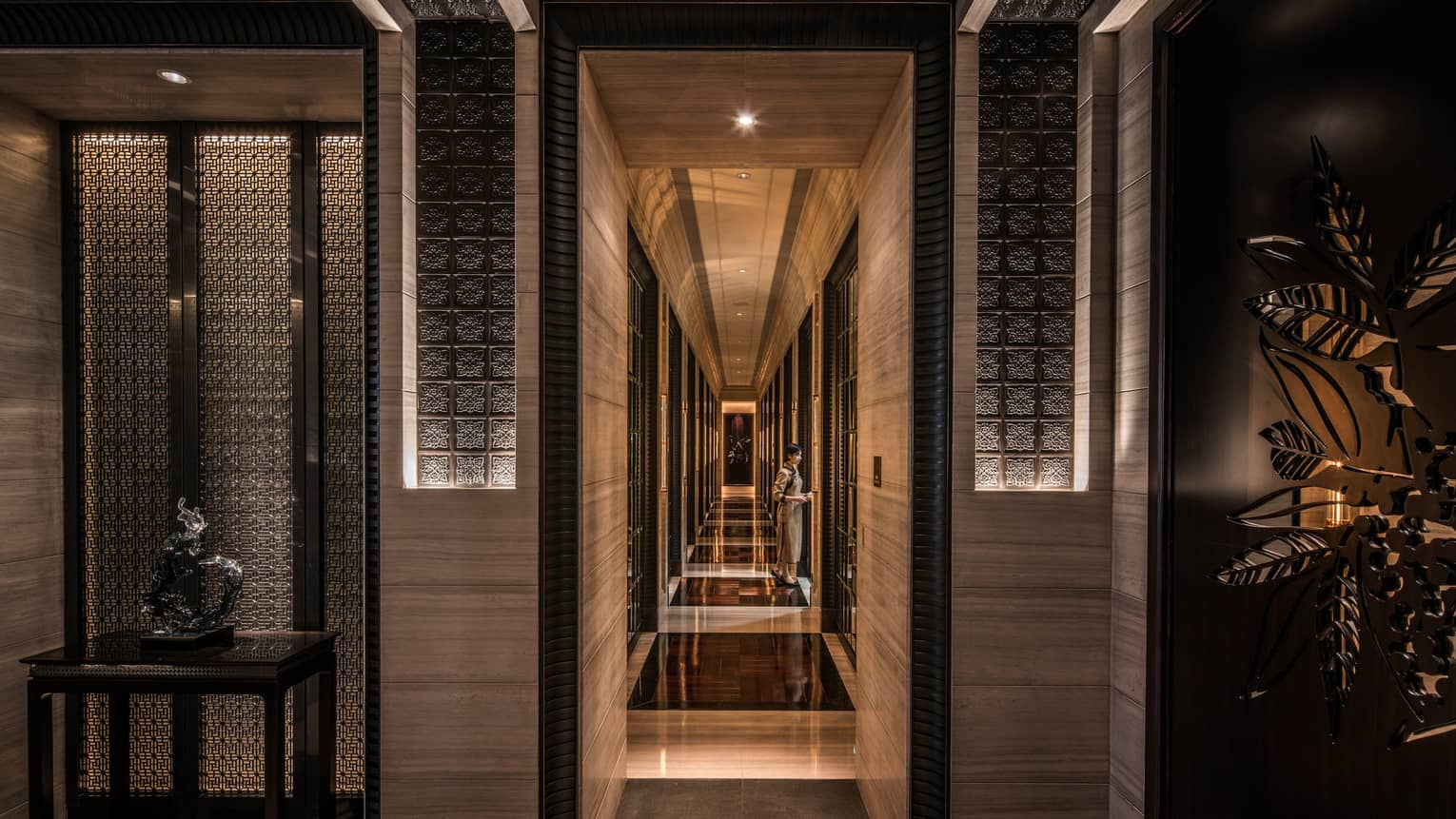 Sculptures, woman at end of long dimly-lit hallway with sleek, wood-grain walls