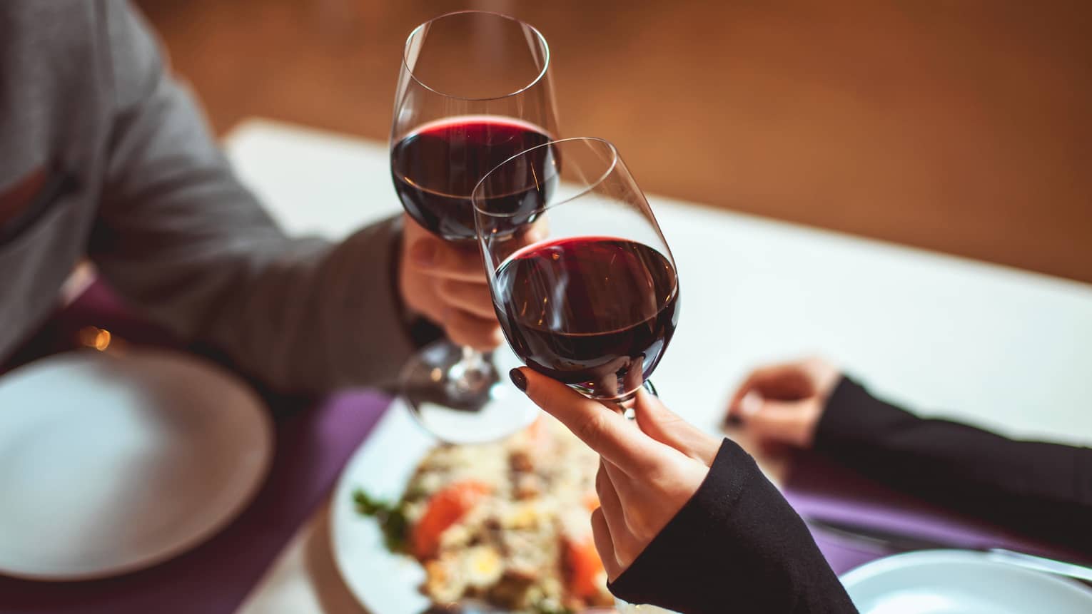 Couple toast with red wine glasses at dining table
