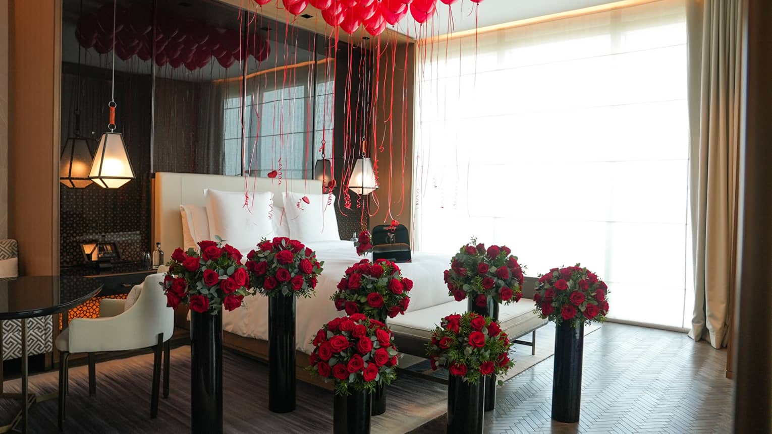 Hotel guest room decorated with bouquets of red roses and red balloons floating over the bed