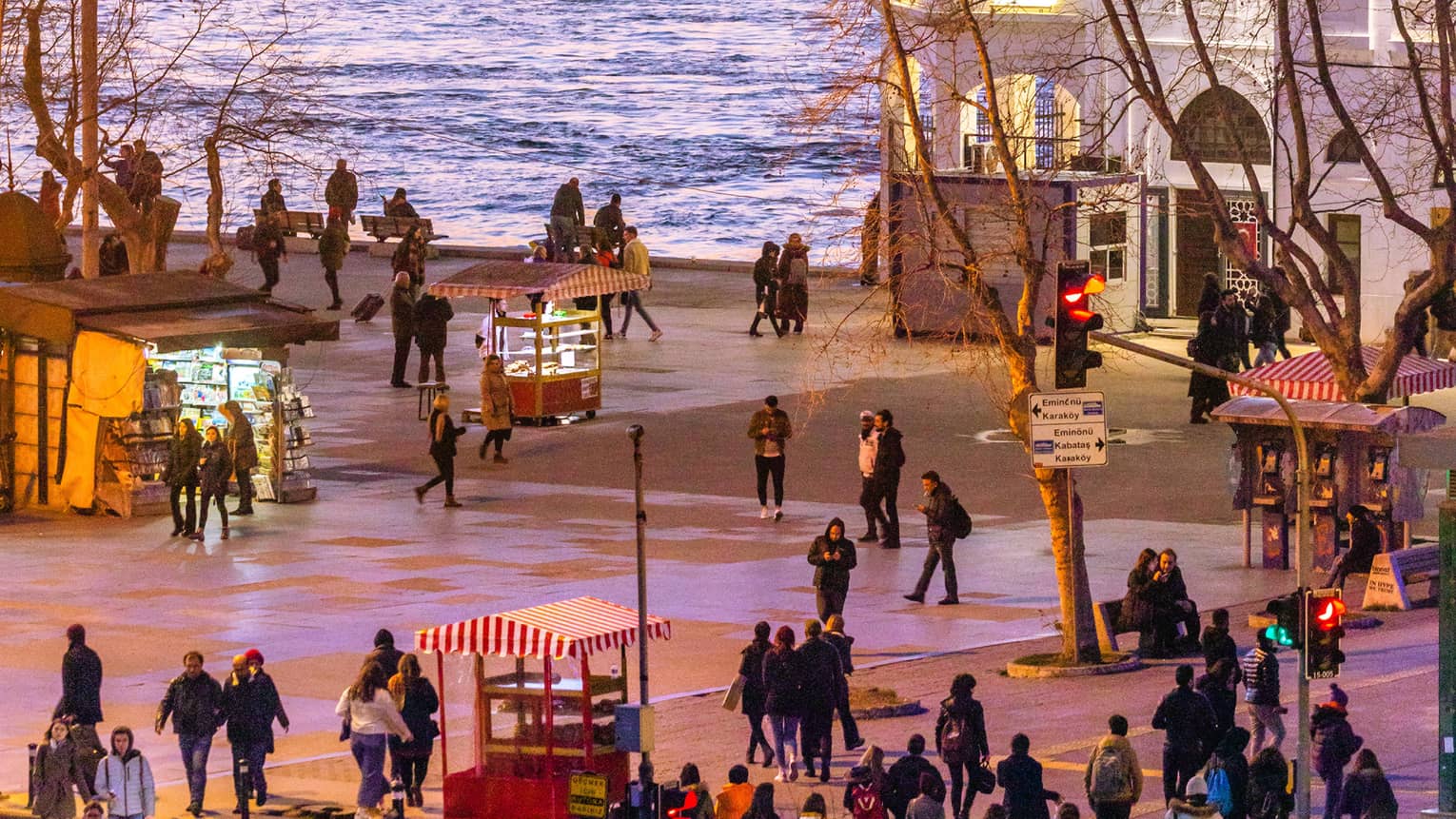 Orange sunset over ferry boat and water, as people stroll the city street