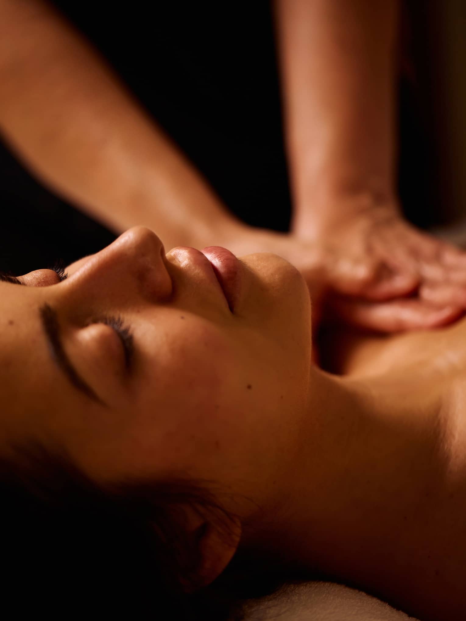 A pair of hands massages the shoulders of a person lying down on their back
