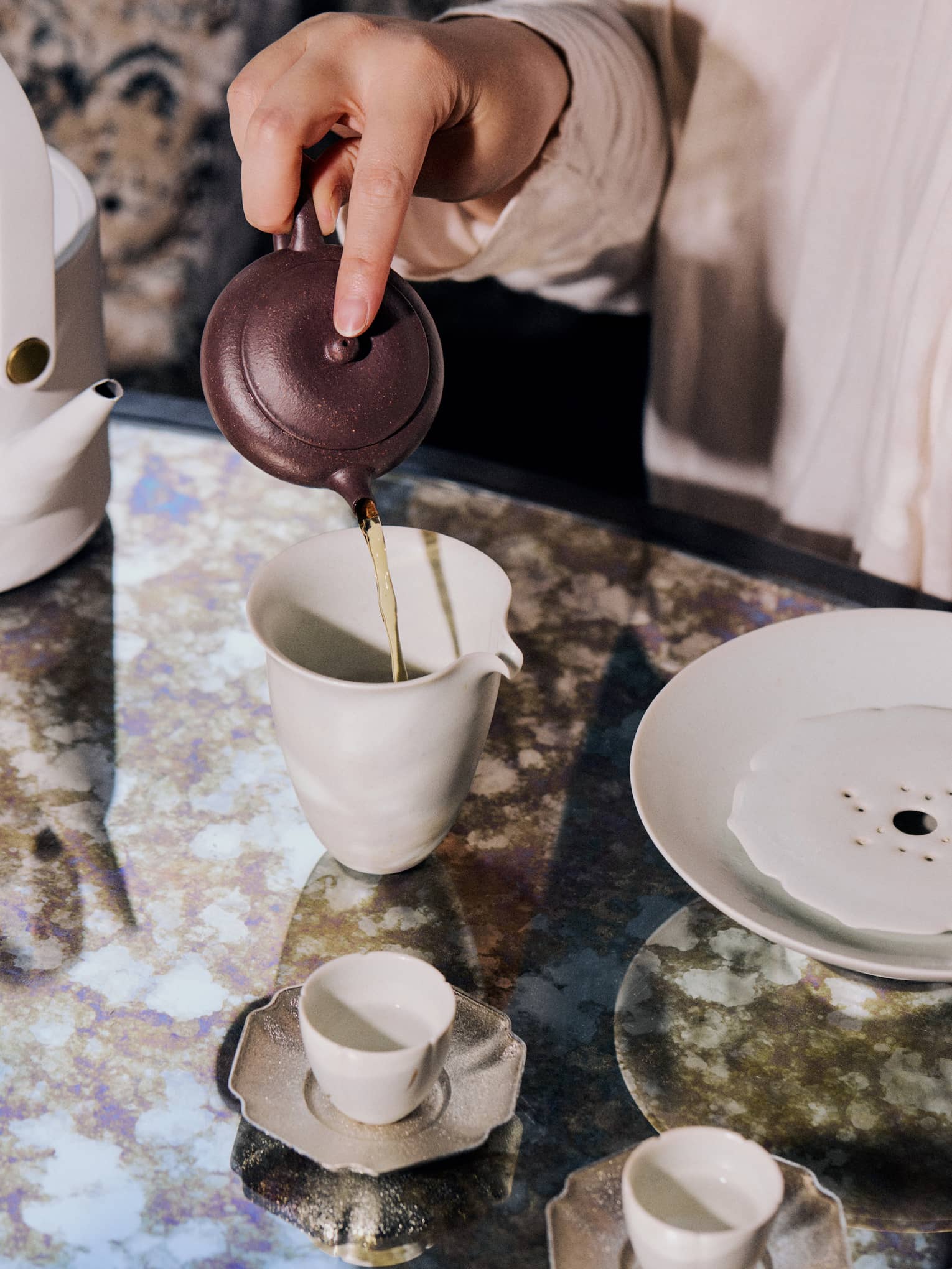 A person pours tea into a white ceramic cup on dining table