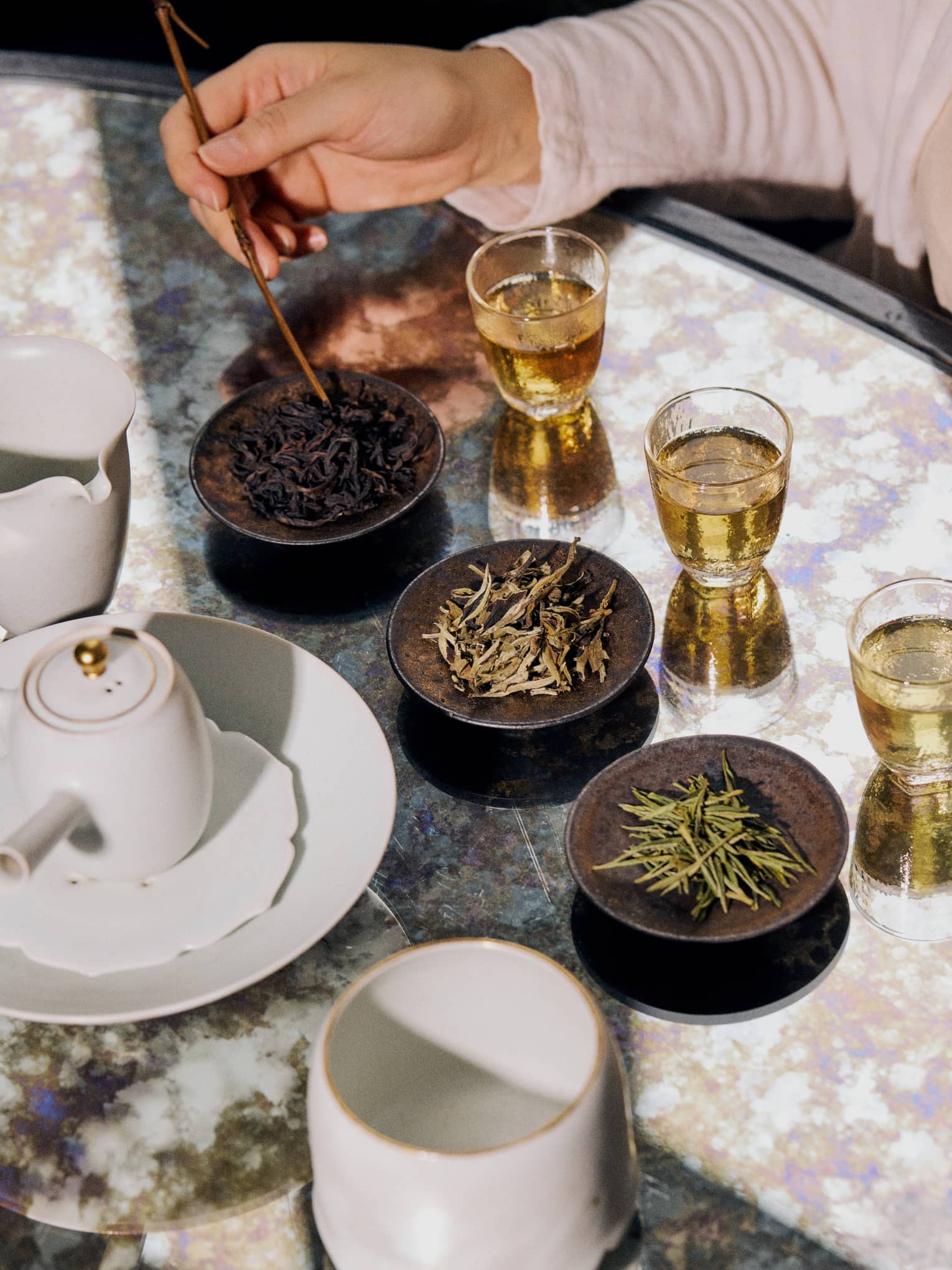 Three brown bowls with various dried tea options alongside three clear glasses of tea.
