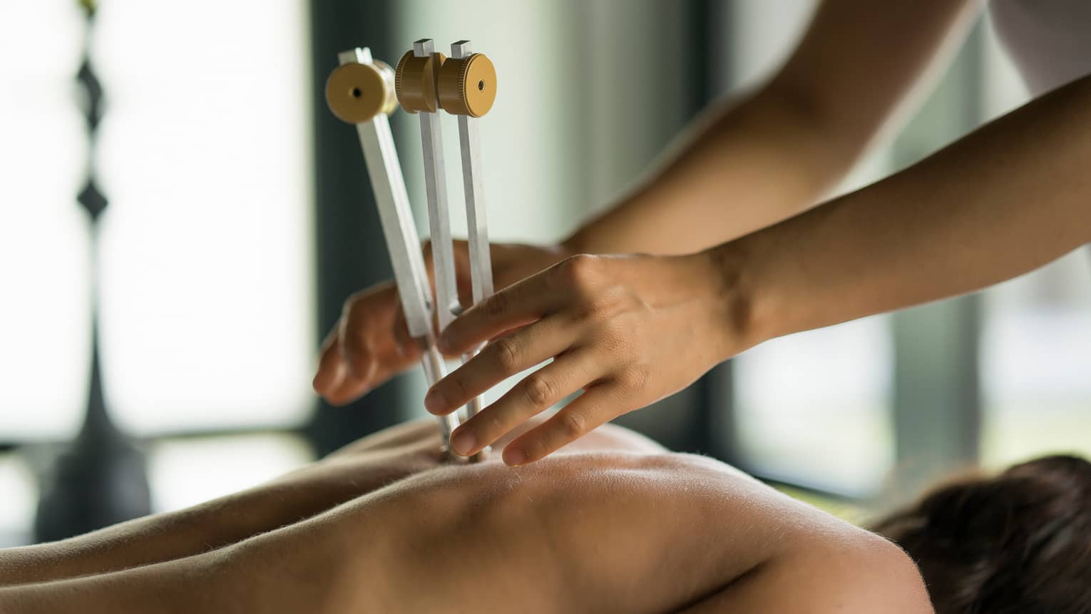 Masseuse uses wood tool on woman's spine, bare back in spa