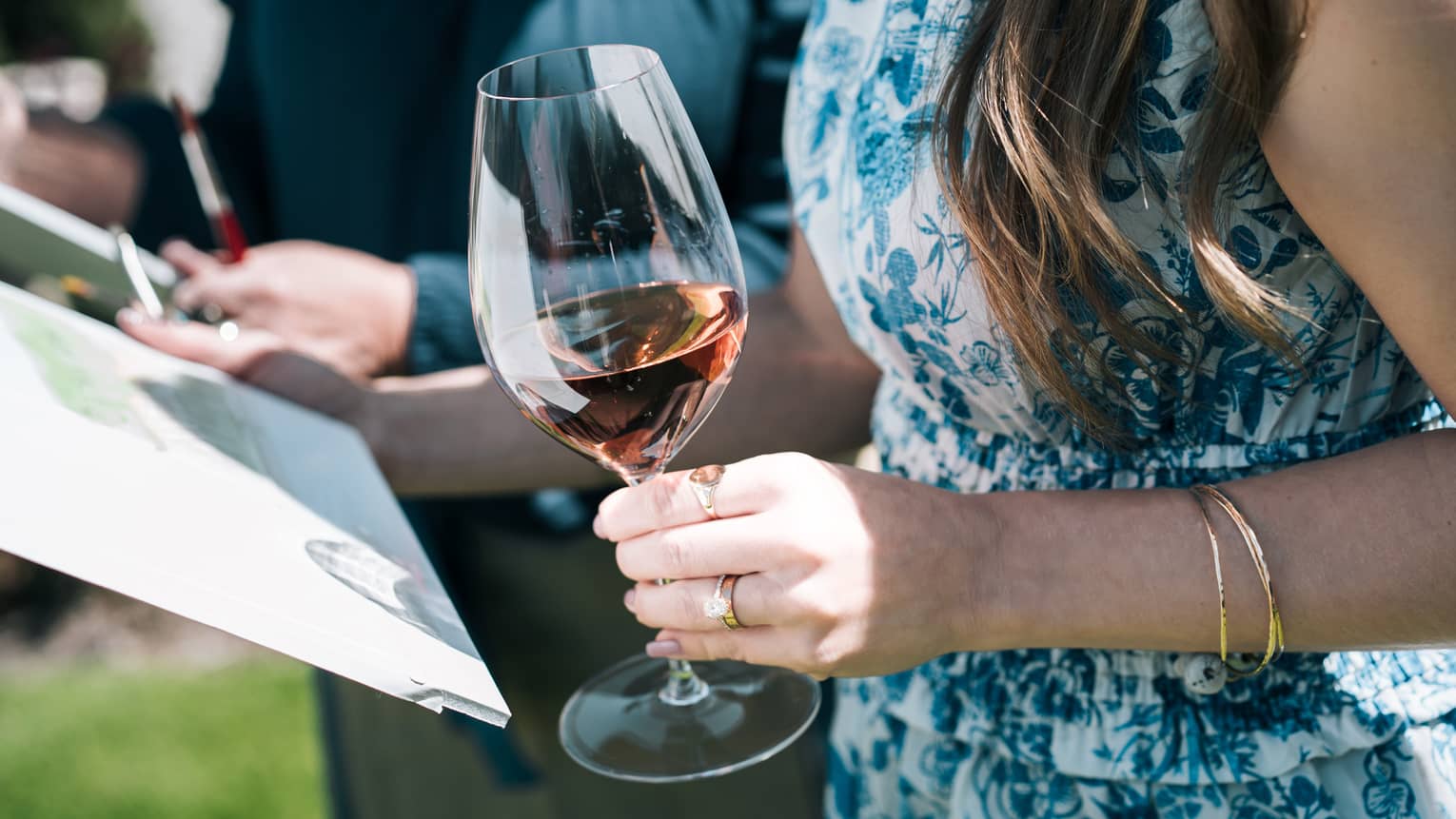 Person holds a glass of wine in one hand while holding a painting in the other