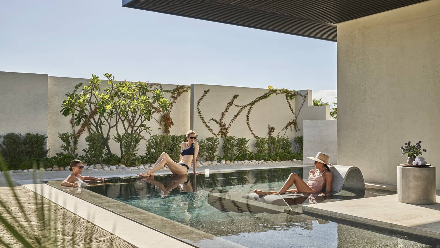 Three women lounging around a small outdoor pool.