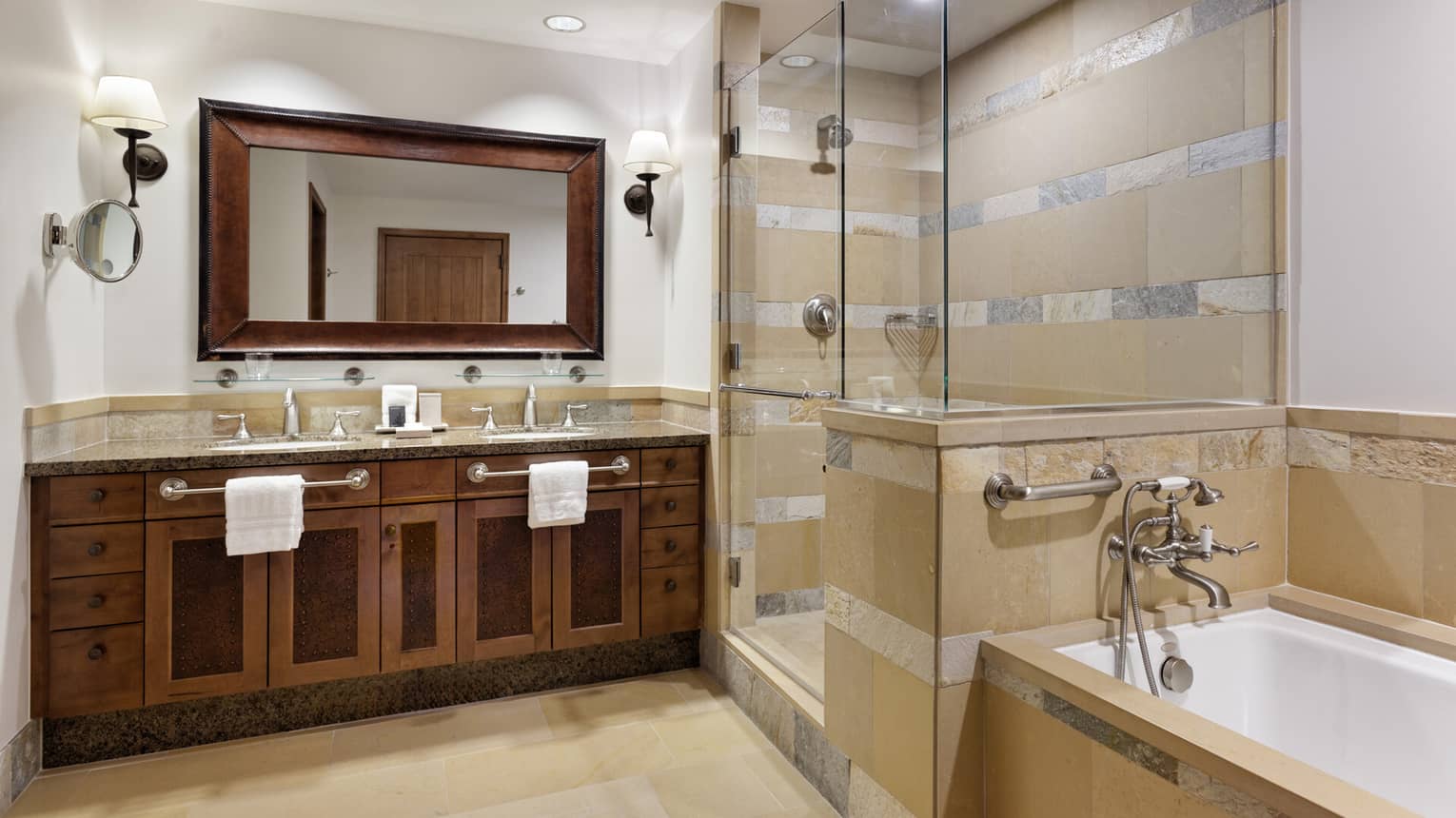 Luxury bathroom with dual-sink vanity with framed mirror and dark wood accents, glass-enclosed shower, and separate bathtub 