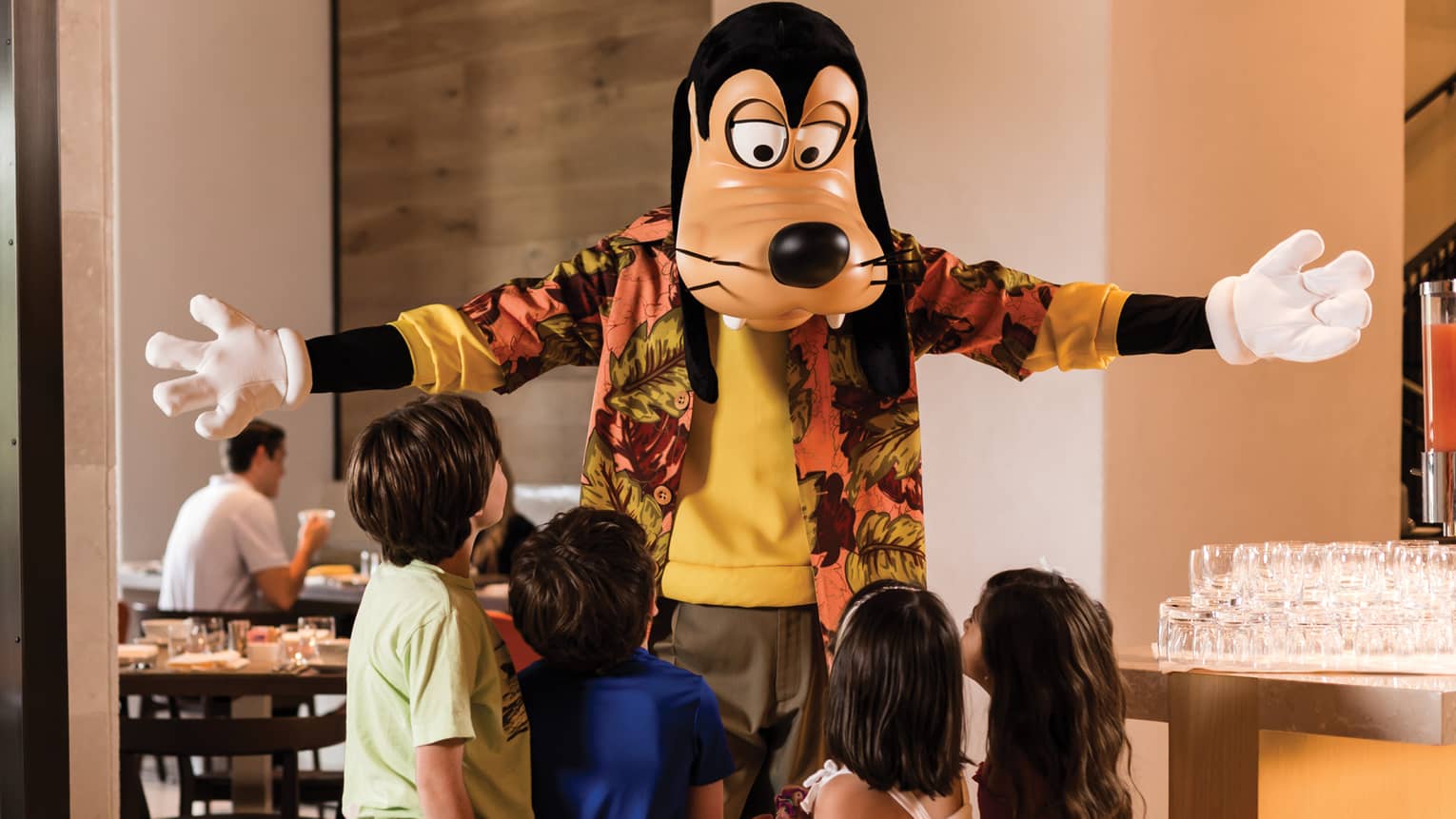 Goofy with four guests in a dining room. 