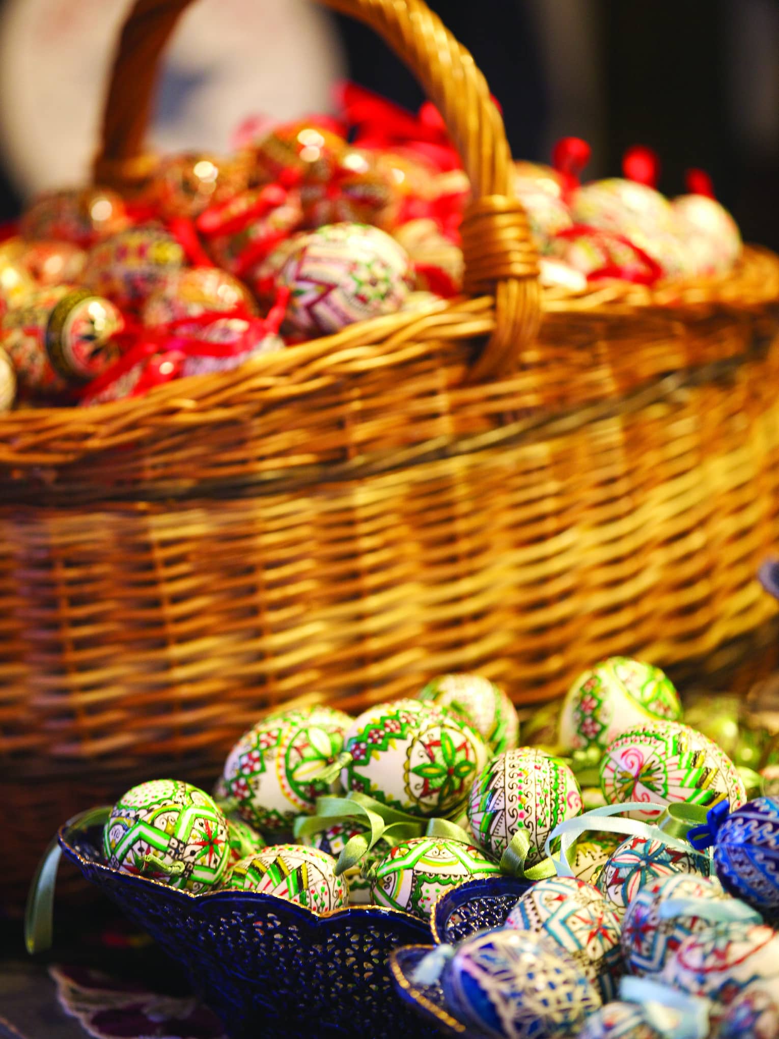Wicker basketful of red Easter eggs, two small dishes in front with blue and green eggs