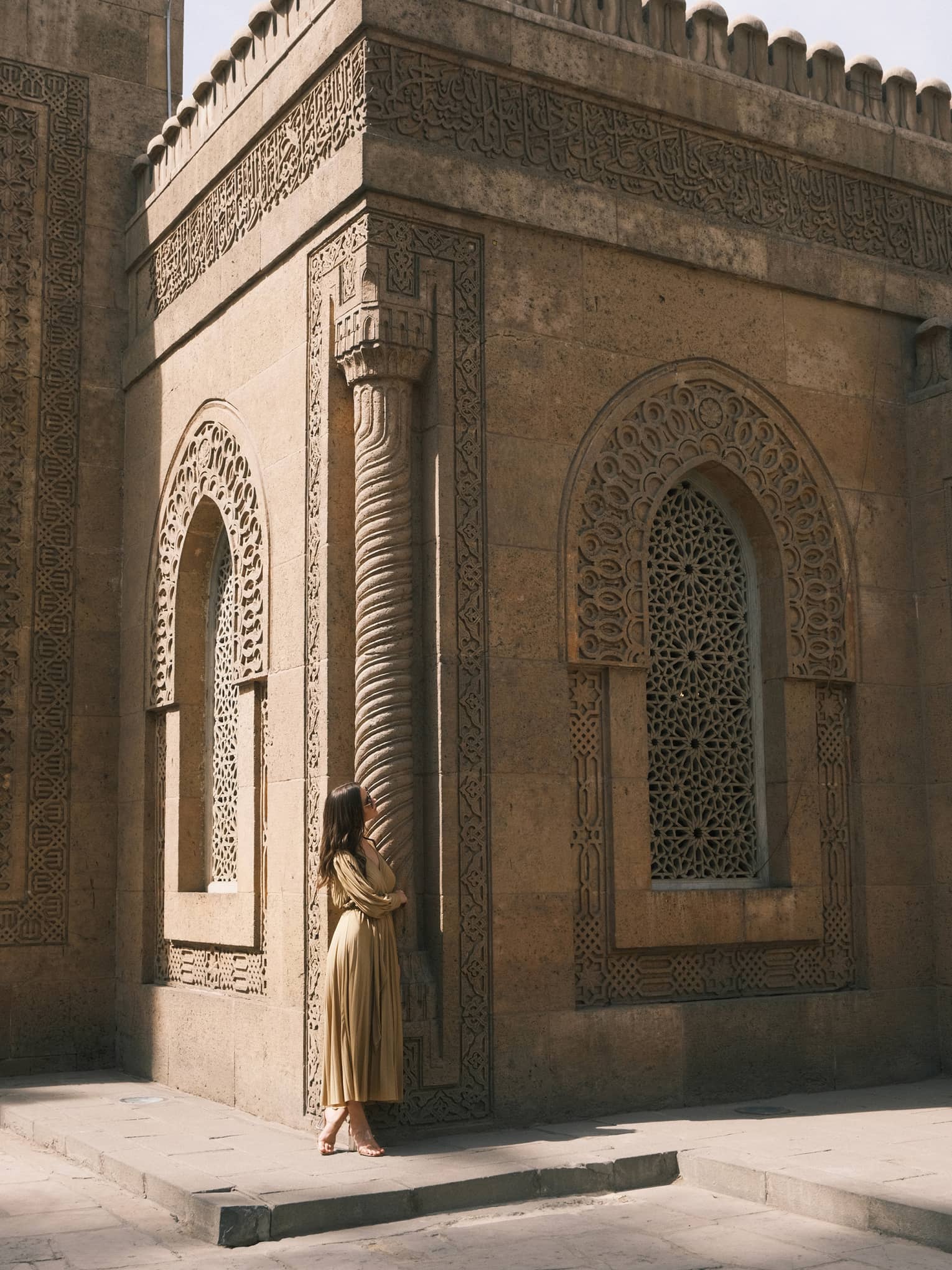 A guest looks up at an ornately carved building featuring a spiral column and arched windows with honeycomb latticework.