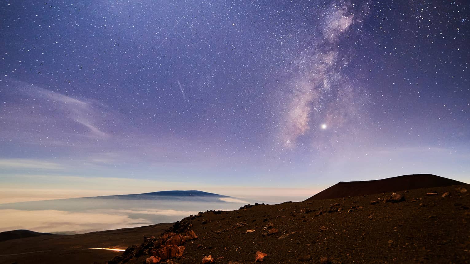 Sunrise under starry sky above mountain, volcanic rocks