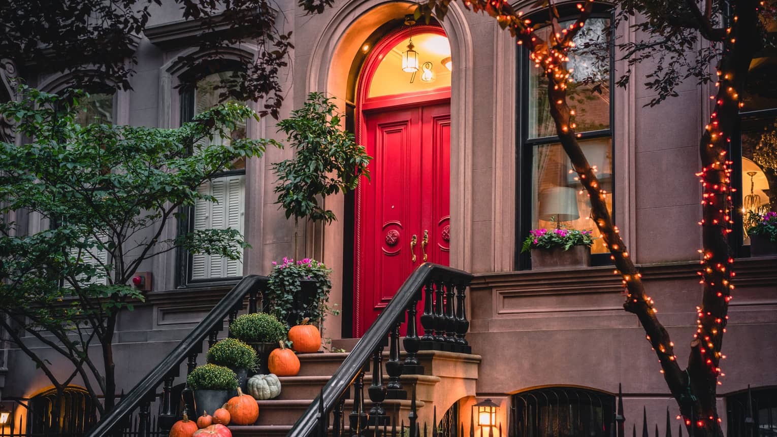 A red door lit by an orange light with pumpkins covering the stairs in front if it.