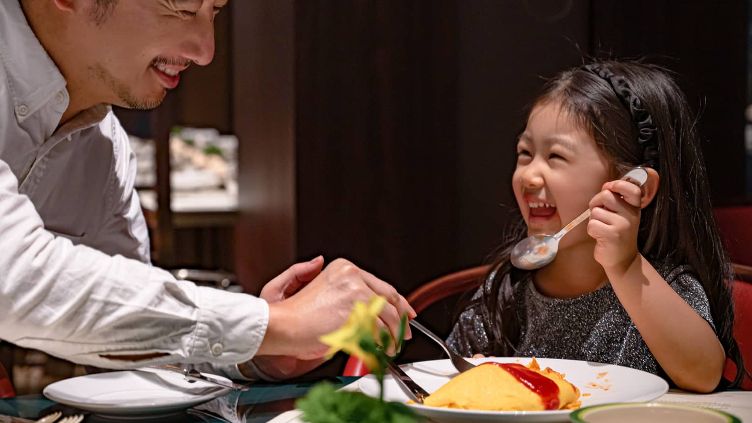 Smiling young girl and her dad dig into omurice topped with ketchup