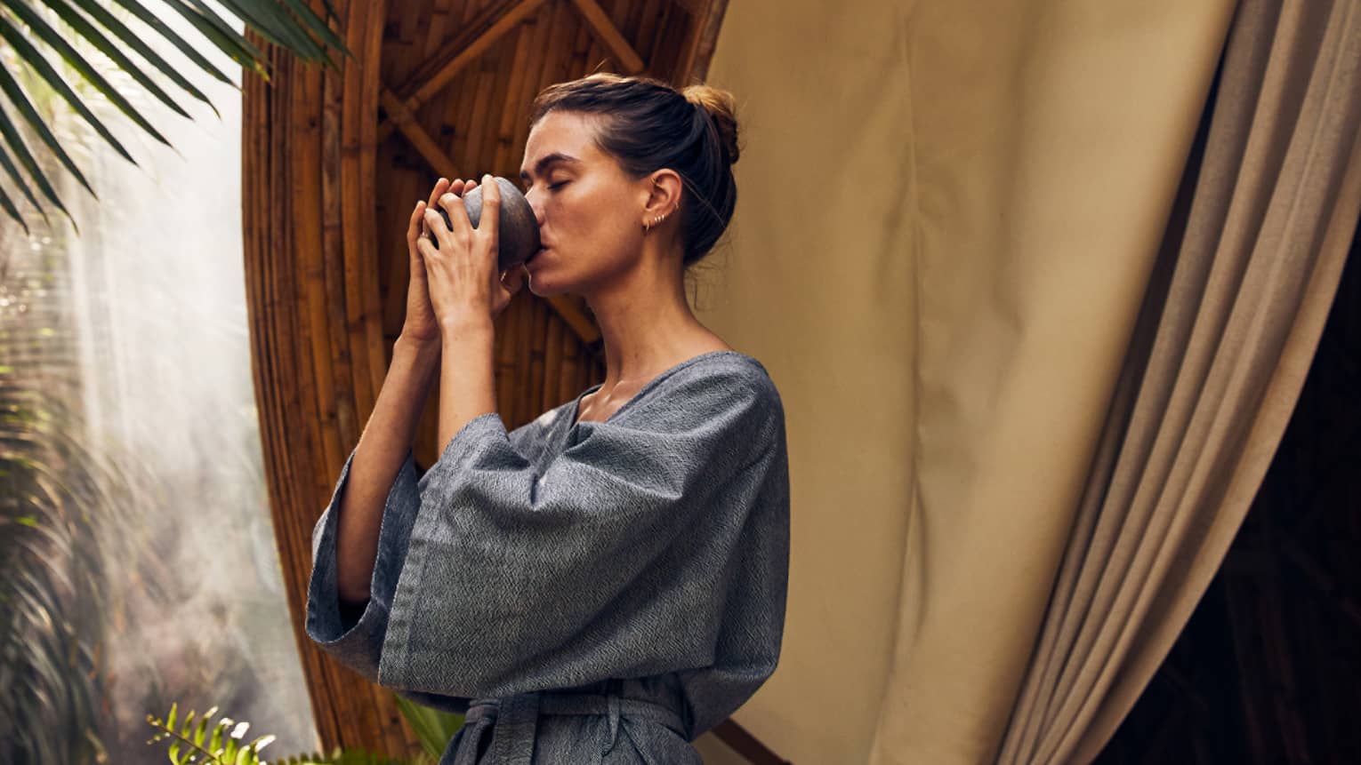 A woman drinking near palm trees and a large spa pod.
