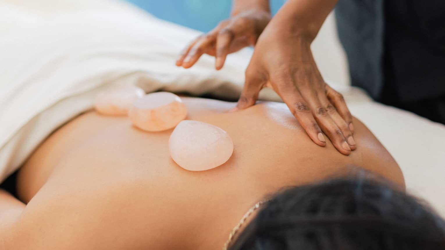 Masseuse places salt stones on a person's bare back