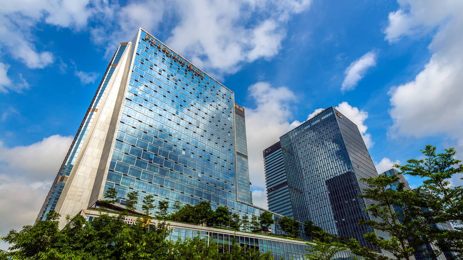 Looking up at Four Seasons Hotel Shenzhen glass towers against blue sky