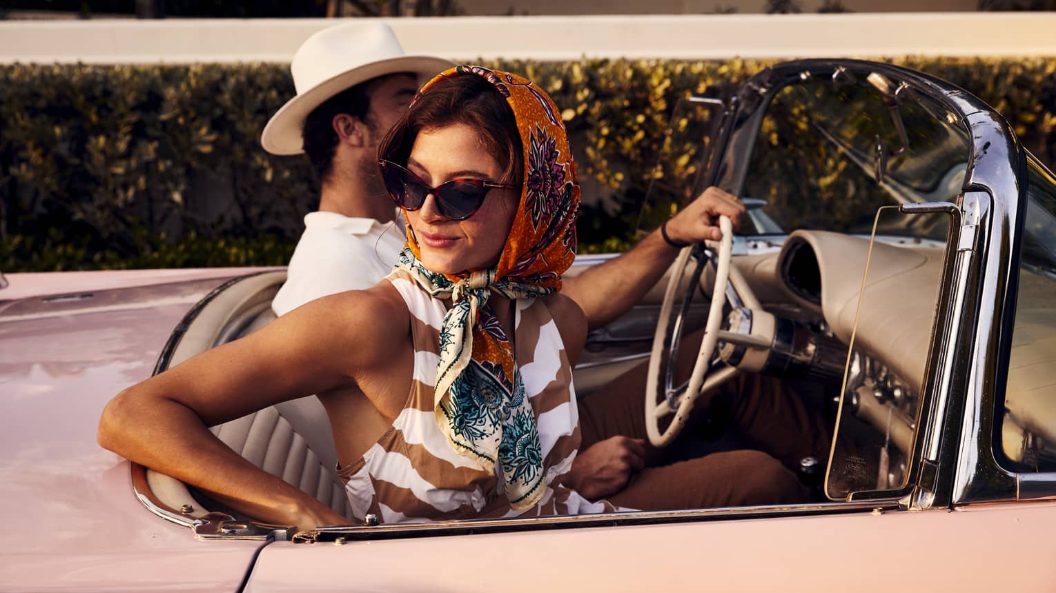 A woman in a scarf and a man in a hat in an old vintage car.