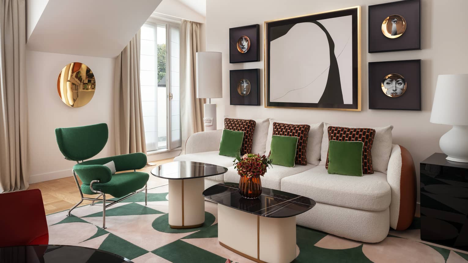 Contemporary hotel suite living room, featuring a sofa with emerald-green and burgundy throw pillows, a green arm chair, and abstract artwork on the wall