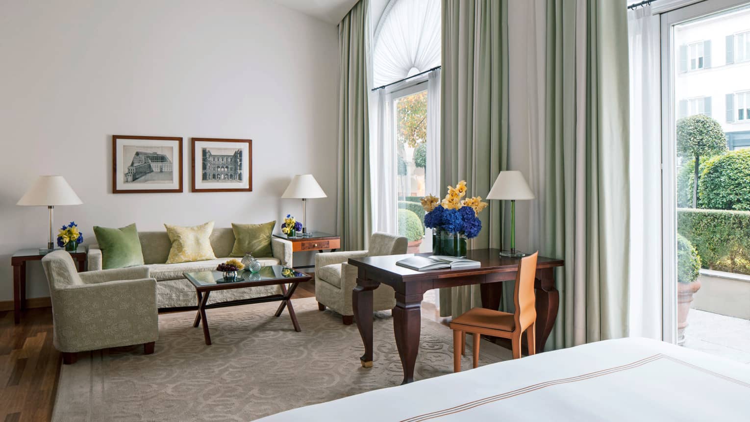 Junior Suite sofa, chairs, wood desk with flowers by two tall sunny windows