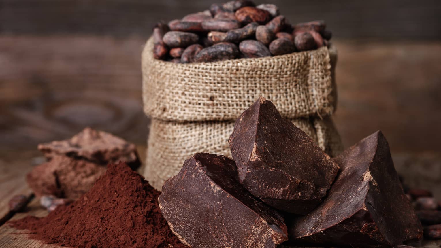 Chunks of chocolate, cocoa powder and coffee beans in a burlap sack