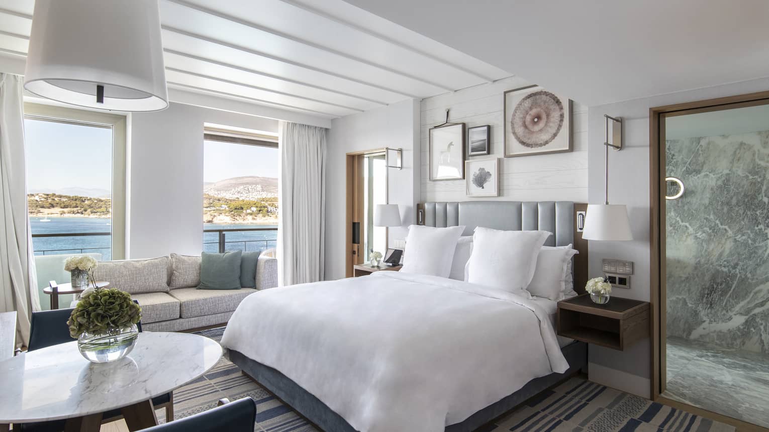Bedroom with king bed, grey headboard, small table and two chairs, sea-view windows